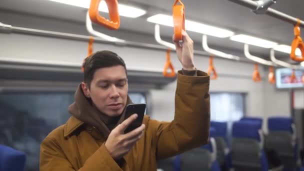 Zblízka pohled pohledný muž stojící ve veřejné dopravě. Interiér přeplněné tramvaje. Muž typy na svém mobilním telefonu. Luxusní Náramkové hodinky. Ležérní oblečení. — Stock video