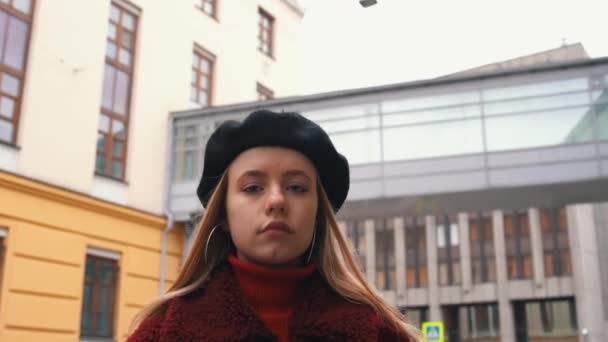 Aantrekkelijke jonge vrouw in de baret op zoek naar de camera op de achtergrond van de stad. Close-up. Portret schot — Stockvideo