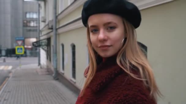 Aantrekkelijke jonge vrouw in de baret op zoek naar de camera op de achtergrond van de stad. Close-up. Portret schot — Stockvideo