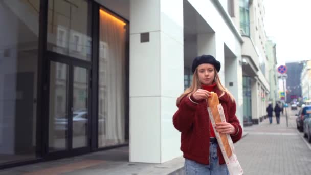 Elegante aantrekkelijke vrouw dragen stijlvolle vacht eten stokbrood in de stad — Stockvideo