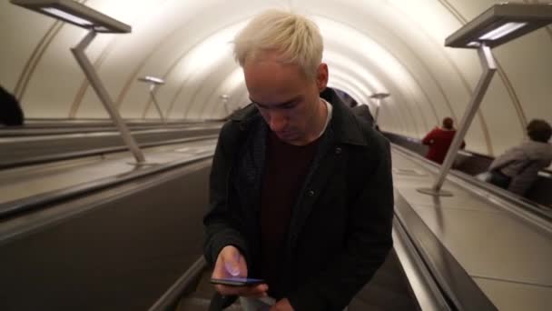 Handsome commuter student man typing a message on the phone going up in escalators. Concept of connection, communication, social media. — Stock Video