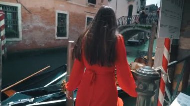 Kırmızı elbiseli genç ve güzel bir kız gondol ve güzel Venedik manzaralı su ile yürüyor