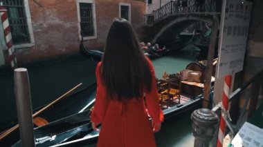 Kırmızı elbiseli genç ve güzel bir kız gondol ve güzel Venedik manzaralı su ile yürüyor