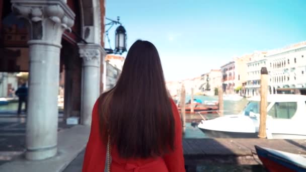 Młoda dziewczyna w czerwonym dresie idzie ulicą i odwraca się. Wenecja, Włochy. — Wideo stockowe