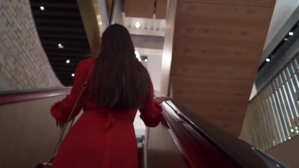 Alışveriş merkezinde yürüyen merdivende duran kırmızı elbiseli genç çekici kızlar, çantalar, alışveriş konsepti, moda konsepti. — Stok video