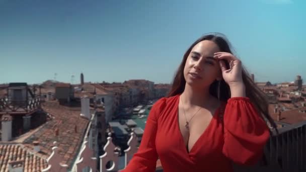 Joven mujer morena hermosa en un vestido rojo sobre un fondo de cielo azul y río, techo Venecia, Italia — Vídeos de Stock
