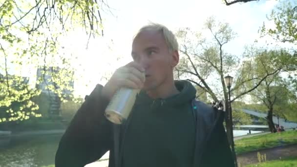 Blond facet picie piwa na tle parku — Wideo stockowe