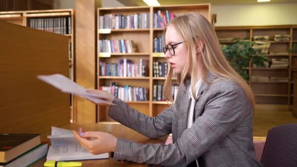 Jonge, verdrietige vrouwelijke student overweldigd door haar huiswerk in de bibliotheek — Stockvideo