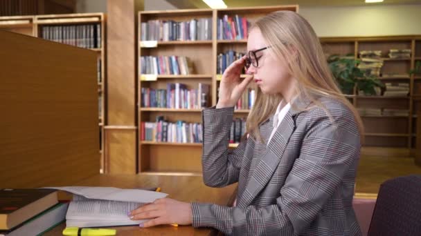 Young, sad female student overwhelmed by her homework in library — 비디오