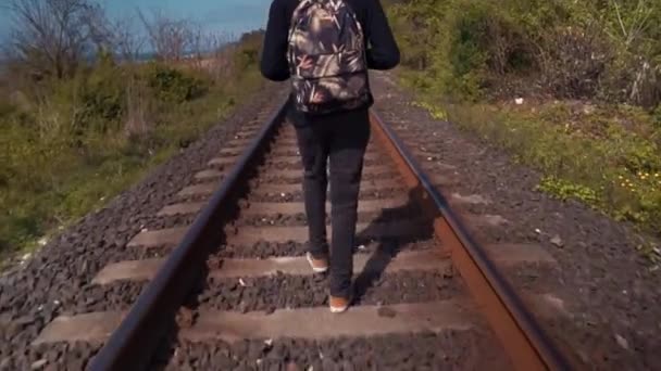 Een man die een rugzak draagt die in de zomer langs een trein spoor loopt — Stockvideo