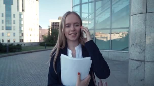 Vista de um lado em uma jovem senhora de negócios andando perto da parede, falando ao telefone — Vídeo de Stock