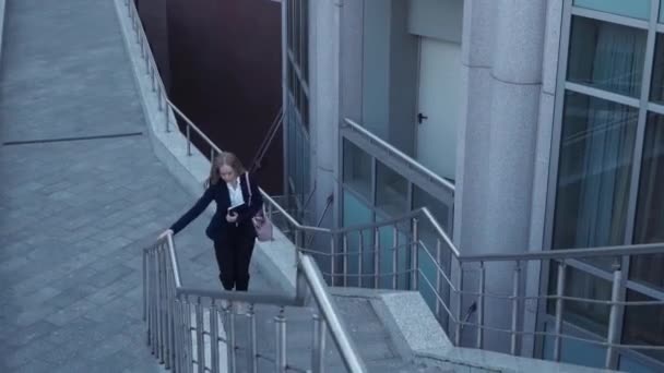 Jonge zakelijke vrouwen in zwarte jas laat en rennen op trap met notebook in handen — Stockvideo