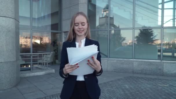 Jeunes femmes d'affaires costume noir regarder les documents papier, sourire et les jeter dans les airs. Bâtiment en verre moderne et contemporain sur fond — Video