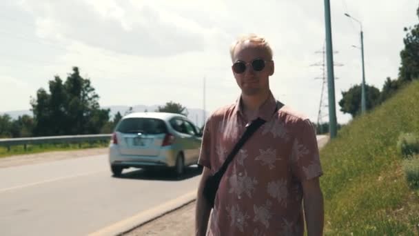 Ragazzo con lo zaino che cammina lungo la strada. Autostop. Tenendo il pollice in alto. Estate giornata di sole . — Video Stock