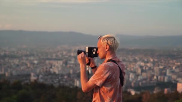 Hipster tourne une vieille caméra de cinéma vintage à l'extérieur dans un parc d'automne doré. Garçon heureux d'essayer de faire son propre film vidéo avec caméra rétro . — Video