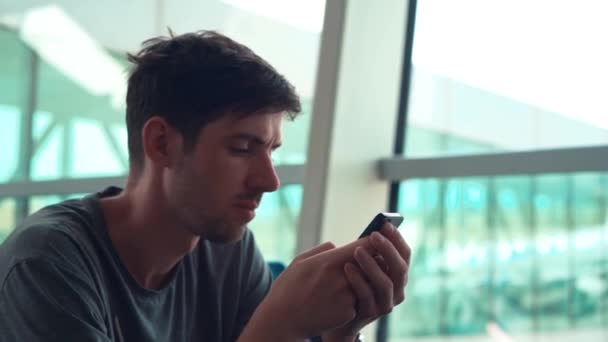 Грустный человек, использующий смартфон в аэропорту — стоковое видео