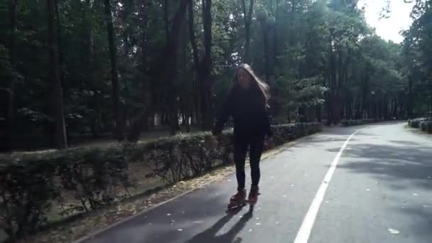 Mano blanca chica de pelo castaño en pantalones negros ajustados mujer montando patines en el parque, durante el día de verano — Vídeo de stock