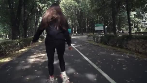 Blanc handsom fille aux cheveux bruns en pantalon noir serré femme équitation patins à roulettes dans le parc, pendant la journée d'été — Video