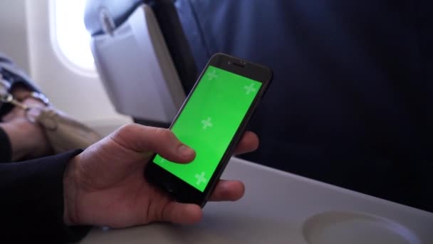 Bir uçakta bir erkek yolcu çekim yakın, kaydırma ve yeşil akıllı telefon ekranı boyunca parmaklarını sürgülü — Stok video