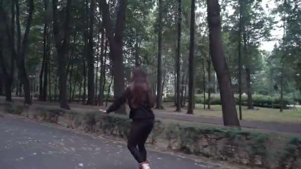 白色手棕色头发的女孩在紧身黑色裤子妇女骑轮滑在公园,在夏季白天 — 图库视频影像