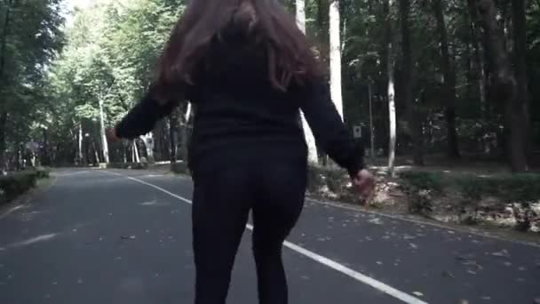 Bianco handsom marrone ragazza capelli in pantaloni neri stretti donna pattini a rotelle in parco, durante il giorno d'estate — Video Stock