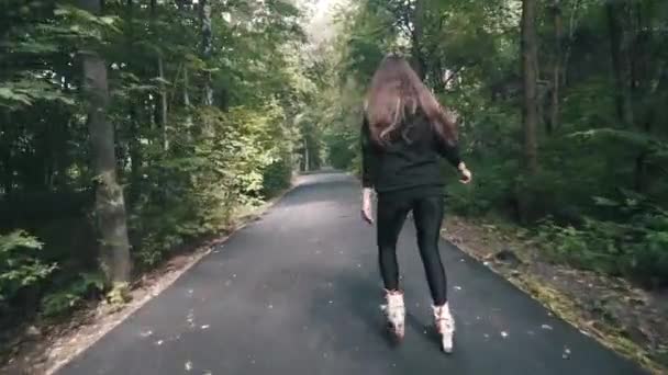 Mano blanca chica de pelo castaño en pantalones negros ajustados mujer montando patines en el parque, durante el día de verano — Vídeo de stock