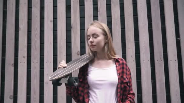 Csípő lány gazdaság gördeszka előtt fa fal — Stock videók