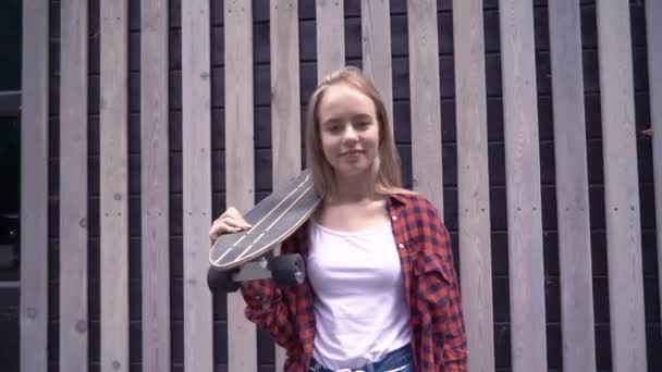 Hipster flicka som håller skateboard framför trä vägg — Stockvideo