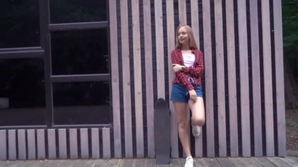 Hipster chica sosteniendo monopatín en frente de la pared de madera — Vídeos de Stock