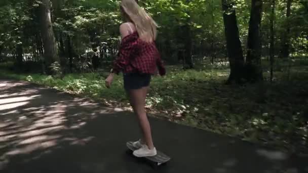 Chica joven monta un monopatín en la calle en un parque de verano — Vídeo de stock