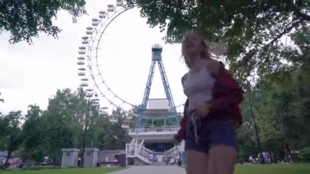 Une jeune femme court dans le parc sur fond de grande roue — Video