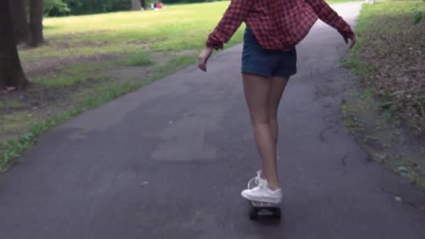 Νεαρό κορίτσι βόλτες με ένα σκέιτμπορντ στο δρόμο σε ένα καλοκαιρινό πάρκο σε αργή κίνηση — Αρχείο Βίντεο