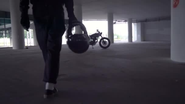 Un motard marchant à travers le parking jusqu'à sa moto. Motocycliste et moto vintage des années 1970. Vue de face arrière scène de style de vie urbain . — Video