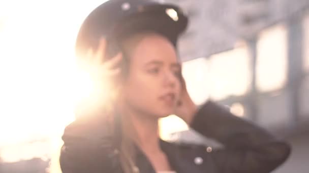 Close-up van jonge motorrijder vrouw zetten retro helm in de buitenlucht bij zonsondergang. Biker meisje in lederen jas dressing voor reis. Vooraanzicht, slow mo — Stockvideo