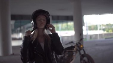 Bir motosikletin yanında güzel bir Beyaz kızın şehir portresi. Deri ceket muhteşem sarışın kadın, motosiklet kask kapalı alarak, sonra gülüyor, tren arka plan