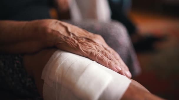 Старая женщина, больная с травмой ноги лежит на больничных носилках дома. Пожилая женщина с гипсом на ноге ждет осмотра. Рука закрывается. . — стоковое видео