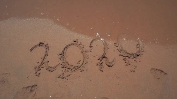 De inscriptie "2020" op het zand wordt weggewassen door de zee Golf. nummers op het zand op het strand van de zee. Gelukkig Nieuwjaar 2021 komt Nieuwjaar 2021, ter vervanging van het jaar 2019. Concept-Nieuwjaar — Stockvideo