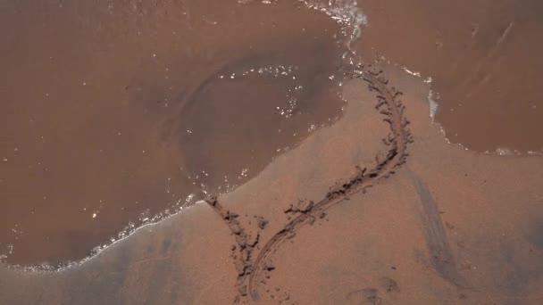 A onda do mar apaga as inscrições escritas na areia . — Vídeo de Stock