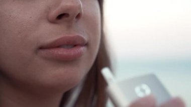 Kırmızı elbiseli, deniz arka plan lı aletli tütün ısıtıcısıyla sigara içen kız. Yakın çekim