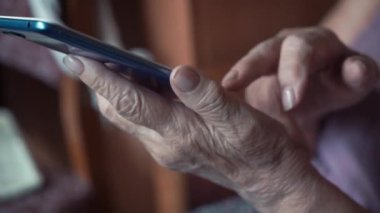Cep telefonu tutan büyükannenin eski elleri. Büyükanne akıllı telefon kullanıyor ve bakıyor. Yakın çekim