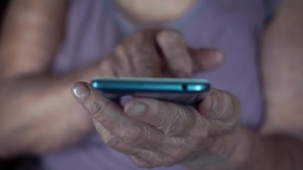 Viejas manos de abuela sosteniendo un teléfono móvil. Abuela usando y mirando el teléfono inteligente. De cerca. — Vídeos de Stock