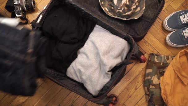 Young man with strong arms packs his suitcase full of manly artisanal items like selvedge denim, flannel shirt, stainless flask and other hipster accessories. Top view — Stock Video