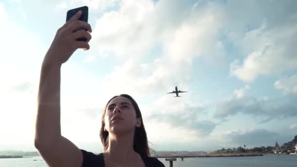 Menina bonita tira uma selfie com o avião no telefone. Viagens blogueiro menina — Vídeo de Stock