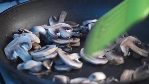 Matlagning en härlig maträtt med stekt svamp, omrörning stek skivor av svamp med en grren sked ugn en keramisk Häll, närbild — Stockvideo