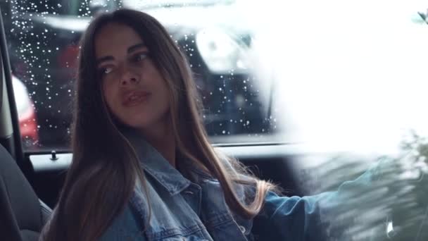 高価な車の車輪の後ろに座っているデニムジャケットに身を包んだ若い魅力的な女性 — ストック動画