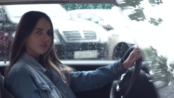 Tânără femeie atractivă îmbrăcată într-o jachetă din denim care stă la volanul unei mașini scumpe — Videoclip de stoc