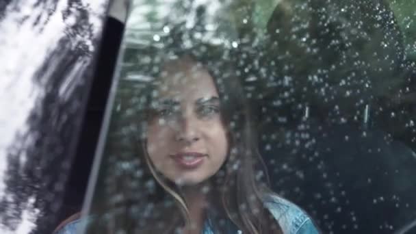 Giovane donna attraente è seduta vicino alla finestra. Sta piovendo fuori dalla finestra. Ritratto di una bella ragazza che guarda la macchina fotografica e apre la finestra — Video Stock