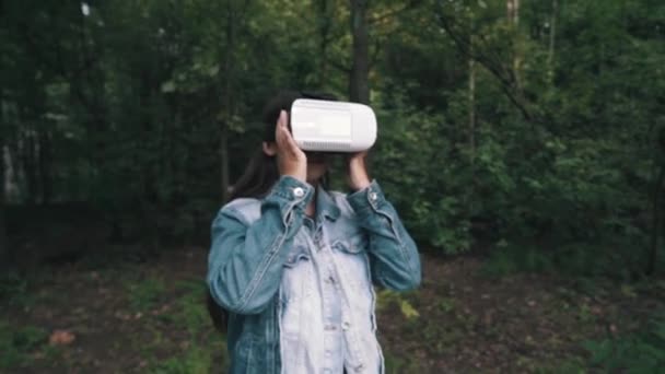 Mladá žena, která nosí ve VR brýle, sluchátka s mikrofonem, hraní virtuálních her a sledování videí venku v parku — Stock video