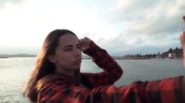 Gün batımında sahilde akıllı telefonla selfie çeken güzel genç kadının portresi