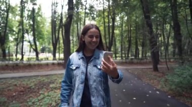 Genç güzel kadın yaz parkında Jean ceket yürüyüş phome tarafından arıyor. görüntülü arama